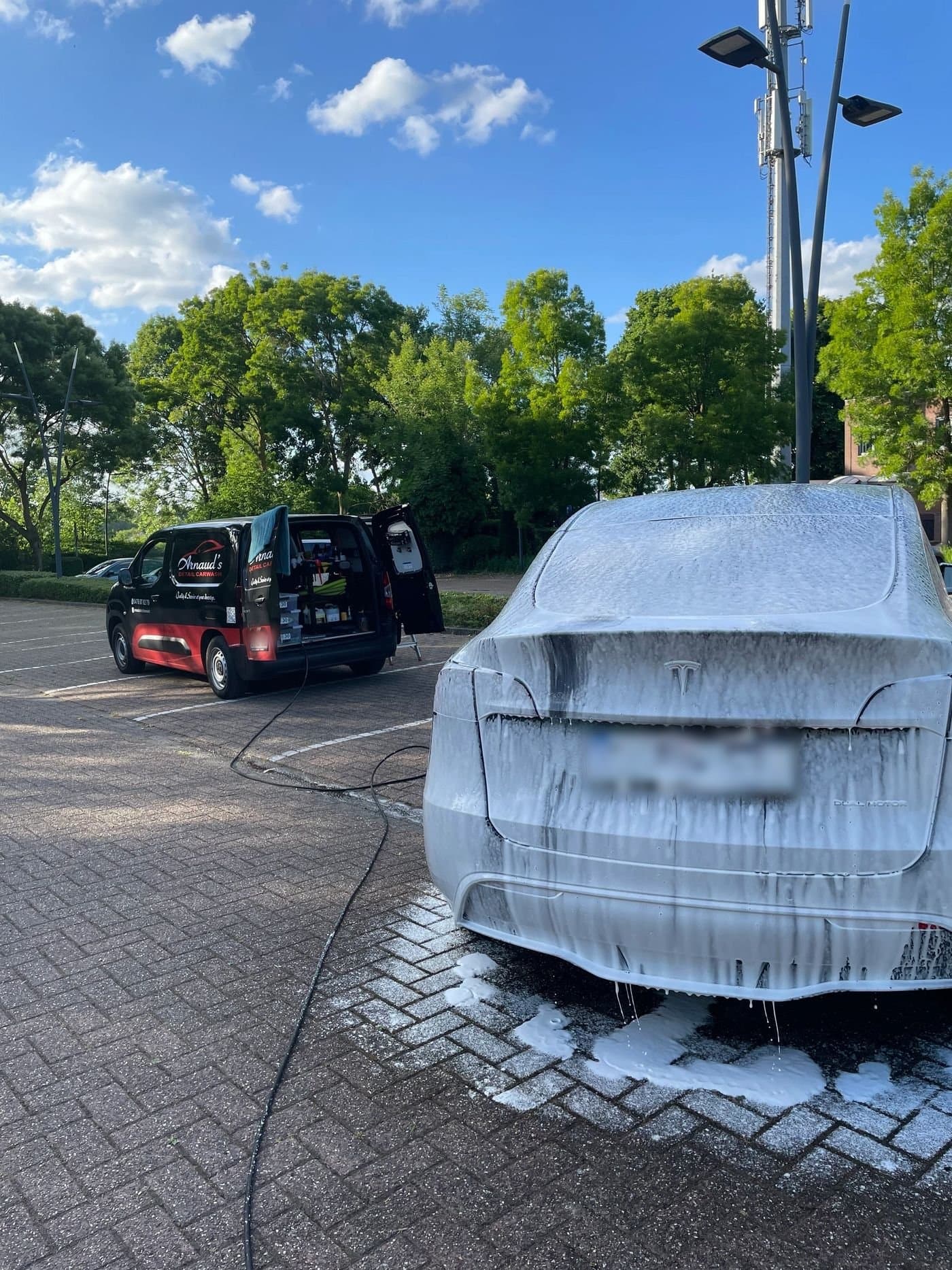 Ein weißes Auto unter Schaum bei einer Handwäsche, im Hintergrund der Transporter von Arnaud's Detail Carwash